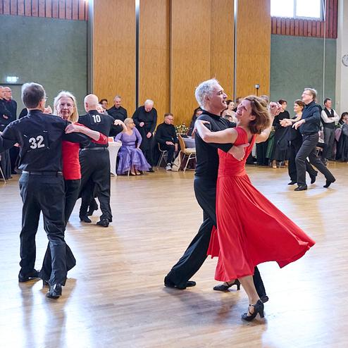 Tanzende Paare in eleganter Kleidung auf einer Tanzfläche bei einer festlichen Veranstaltung. Stolze Atmosphäre im Hintergrund.