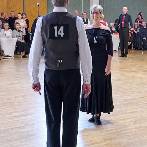 Tanzpaar auf einer Tanzfläche, Mann mit der Nummer 14 und Frau in schwarzem Kleid stehen sich gegenüber.