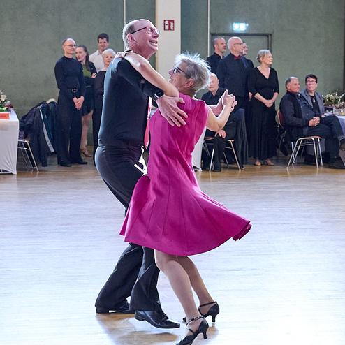 Tanzpaar in eleganter Kleidung, der Mann führt die Frau in einem pinken Kleid auf einer Tanzfläche.