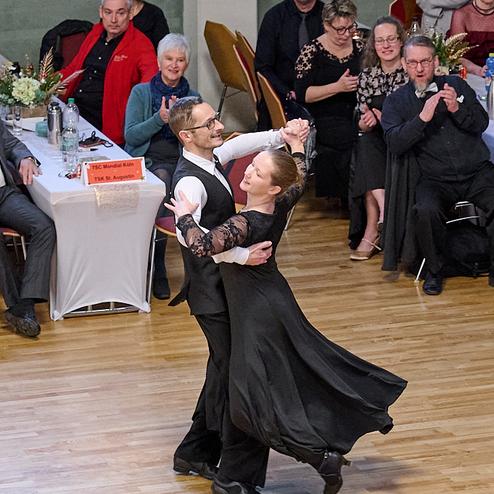 Tanzendes Paar in eleganter Kleidung auf einer Tanzfläche, Zuschauer applaudieren im Hintergrund.