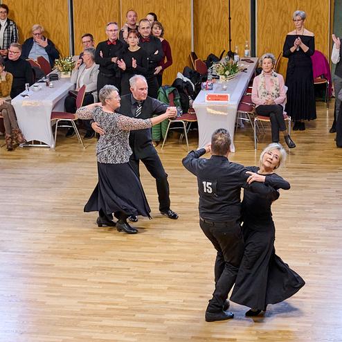 Tanzpaar in eleganter Kleidung führt einen Walztanz auf einer Holz-Tanzfläche vor Publikum auf.
