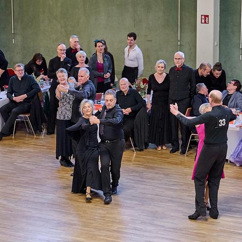 Tanzpaar in eleganter Kleidung auf einer Tanzveranstaltung, umgeben von Zuschauern an festlich gedeckten Tischen.