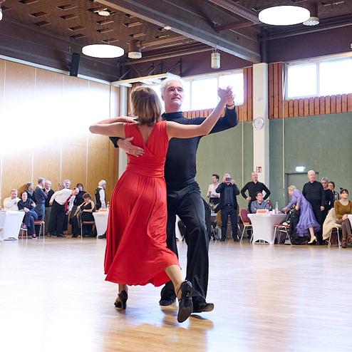 Tanzpaar in eleganter Kleidung führt einen Paso Doble auf einer Tanzfläche vor Publikum in festlichem Saal auf.