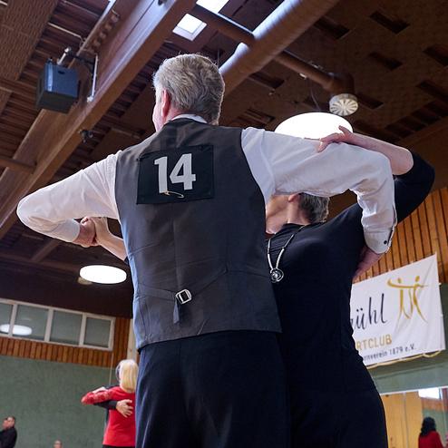 Tanzpaar in eleganter Haltung, der Mann mit Nummer 14 auf dem Rücken, in einer Turnieratmosphäre.