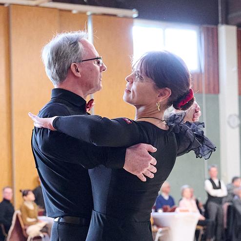 Tanzpaar in eleganter Kleidung während eines Tanzwettbewerbs, umgeben von Zuschauern in einem Festsaal.