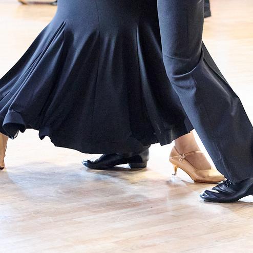 Tanzende Paare zeigen ihre Füße, einer in schwarzen, der andere in beigen Schuhen auf glattem Parkettboden.