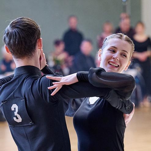 Tanzpaar in eleganter Kleidung während eines Wettbewerbs, lächelnd und in einer tänzerischen Pose auf der Fläche.