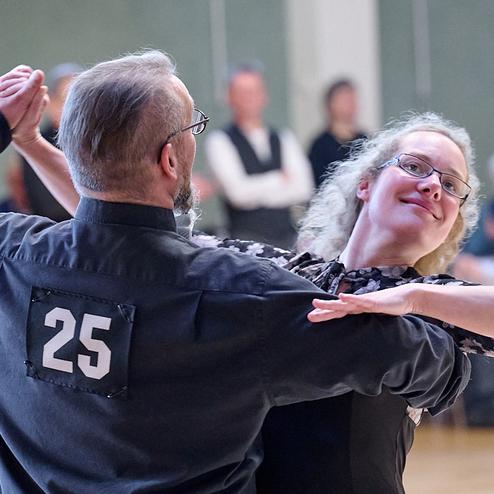 Tänzerisches Paar in eleganter Kleidung bei einem Tanzwettbewerb, Nummer 25 auf dem Rücken des Mannes sichtbar.