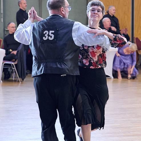 Tanzendes Paar in eleganter Kleidung auf einer Tanzfläche, Blickkontakt und harmonische Bewegung.