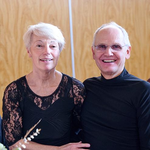 Lächelndes Paar sitzt zusammen an einem Tisch vor hölzernem Hintergrund, dekoriert mit Blumen und einem Geschenk.