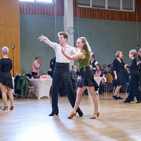 Tanzveranstaltung mit Paaren in eleganter Kleidung, die auf einer Tanzfläche zu Musik tanzen. Tische im Hintergrund.