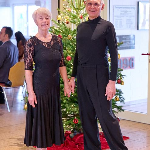 Tanzendes Paar in eleganter Kleidung steht vor einem geschmückten Weihnachtsbaum in festlicher Atmosphäre.