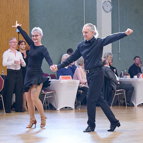 Tanzpaar in eleganter Kleidung zeigt einen Tanz auf einer Veranstaltung, Zuschauer schauen aufmerksam zu.