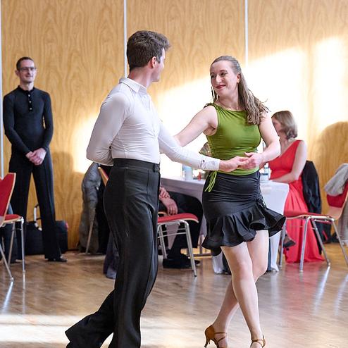 Tanzpaar in eleganter Kleidung bei einem Tanzwettbewerb, umgeben von Zuschauern in einem festlichen Saal.