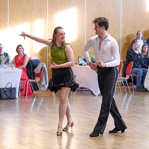 Tanzpaar in auffälliger Kleidung präsentiert einen Paso Doble in einem hellen Saal vor einer Zuschauergruppe.