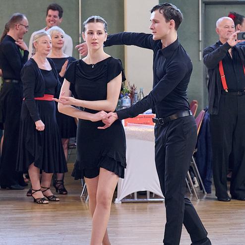 Tanzpaar in eleganter Kleidung führt eine Tanzhaltung in einer festlichen Umgebung aus, im Hintergrund Zuschauer.