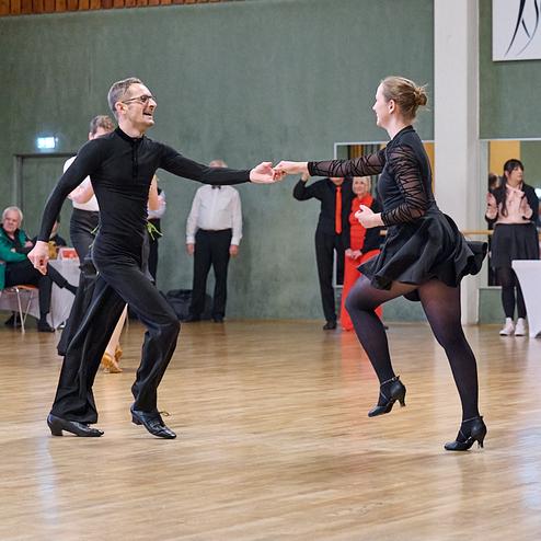 Tanzpaar in eleganter Kleidung zeigt dynamischen Tanz auf einer Holzfläche während des Wettbewerbs.