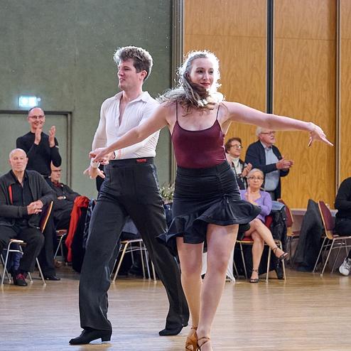 Tanzpaar in eleganter Kleidung führt einen Tanz vor Publikum in einer hellen Sporthalle auf.