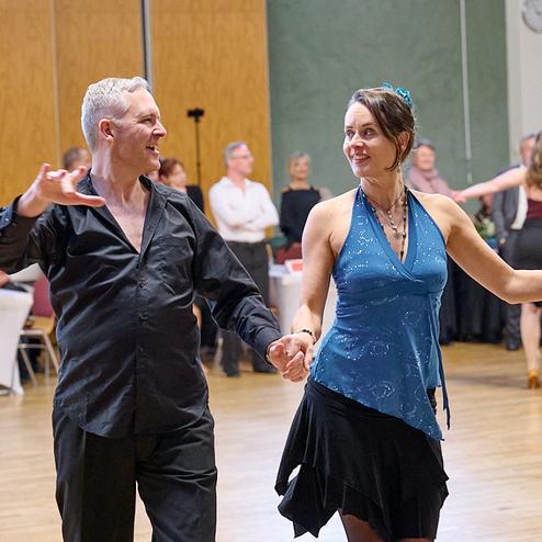 Tanzpaar in eleganter Kleidung führt einen spannenden Tanz auf einer Veranstaltung mit Publikum im Hintergrund.