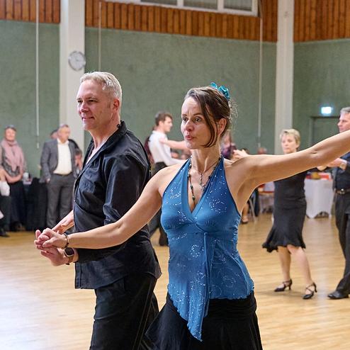 Tanzpaar führt einen leidenschaftlichen Tanz in einem festlichen Saal mit tanzenden Gästen im Hintergrund aus.