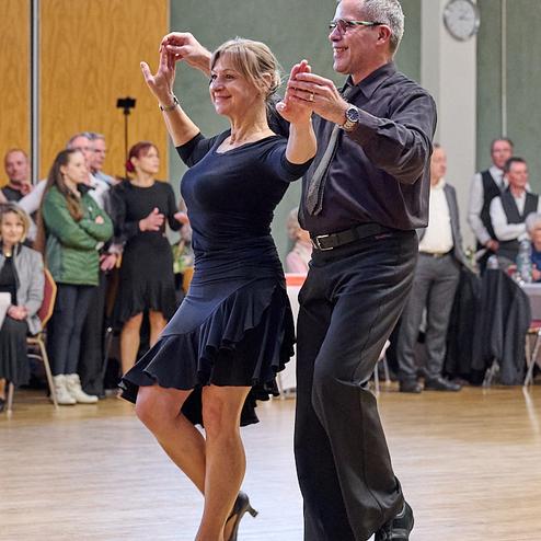 Tanzpaar führt einen Paso Doble auf einer Tanzfläche, umgeben von Zuschauern in festlicher Kleidung.