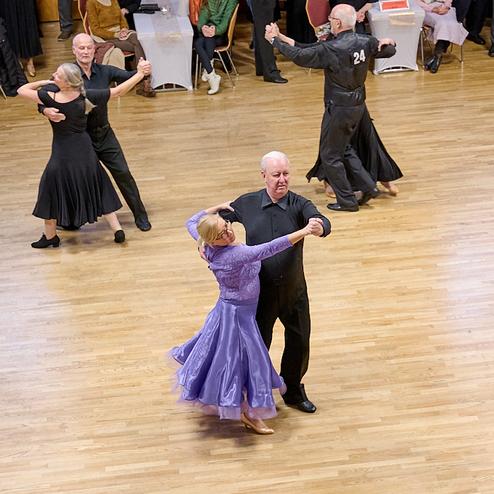 Tanzpaar führt einen Walzer in eleganter Kleidung auf einem Holzparkettboden bei einer Tanzveranstaltung aus.