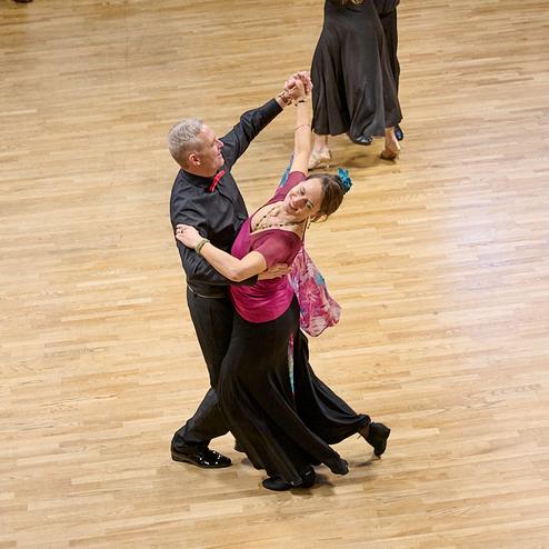 Tanzpaar in eleganter Abendgarderobe tanzt auf einem Holzparkett während einer Veranstaltung in festlicher Atmosphäre.