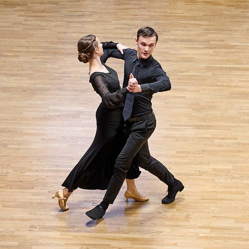 Tanzpaar in eleganter Abendkleidung führt einen Ausdruckstanz auf einer Holzfläche vor Publikum aus.