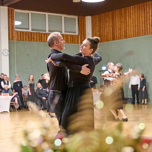 Tanzpaar in eleganter Kleidung führt einen Walzer auf einer Tanzfläche vor einem Publikum aus mehreren Zuschauern aus.