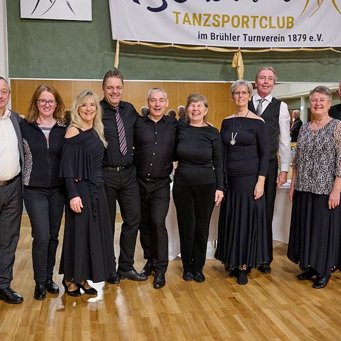 Gruppenfoto von zehn Tänzern in festlicher Kleidung, im Hintergrund eine Tanzfläche und ein Banner des Tanzsportclubs.