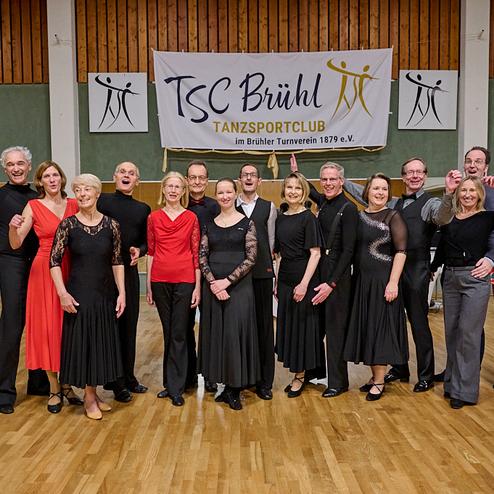 Gruppenfoto von Tänzern in eleganter Kleidung vor einem Banner des TSC Brühl im Tanzsportclub.