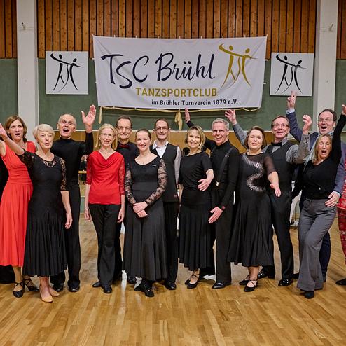 Gruppenshot von Tänzern in festlicher Kleidung beim TSC Brühl, vor einem Banner des Tanzsportclubs.