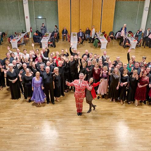 Gruppenshot von älteren Tänzern in eleganter Kleidung, die fröhlich in einem Saal mit Tischen stehen.