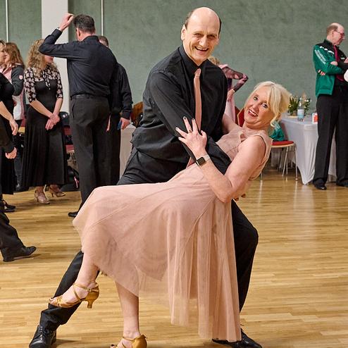 Tanzpaar in eleganter Kleidung führt einen schwungvollen Schritt auf einer Tanzfläche aus Holz aus.