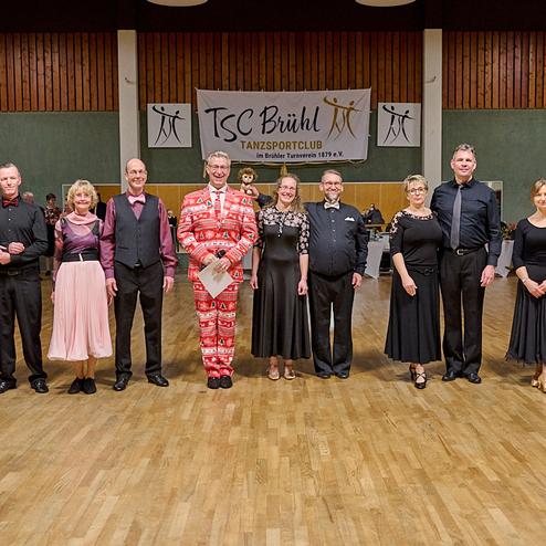 Gruppe von Tänzern in eleganter Kleidung auf einer Tanzfläche mit Vereinsbanner im Hintergrund.