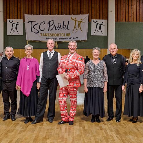 Gruppenfoto von Tänzern in festlicher Kleidung im TSC Brühl Tanzsportclub, vor einem Veranstaltungsbanner.