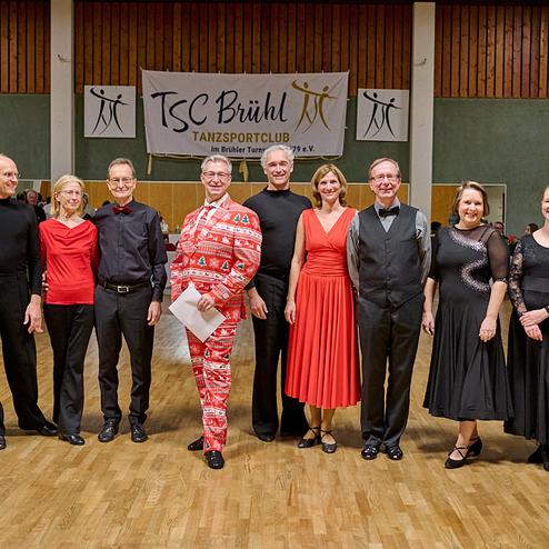 Eine Gruppe von Tänzern in festlicher Kleidung steht auf einer Tanzfläche vor einem Banner des TSC Bühhl.