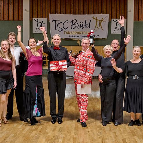 Gruppenszene von tanzenden Personen im Festkleid auf einer Tanzveranstaltung im TSC Brühl, alle mit freudigen Gesten.