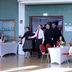 Menschen betreten einen festlich geschm&uuml;ckten Raum, w&auml;hrend mehrere G&auml;ste an Tischen sitzen und zuschauen.