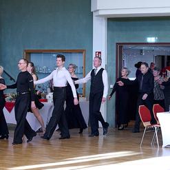 Tanzende Paare in eleganter Abendkleidung bewegen sich durch einen festlich dekorierten Raum.