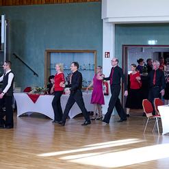 Tanzende Paare in formeller Kleidung bewegen sich durch einen festlich dekorierten Festraum.