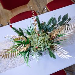 Dekoratives Tischarrangement mit gr&uuml;nen Pflanzen, goldenen Akzenten und Kerzen auf einem wei&szlig;en Tisch.