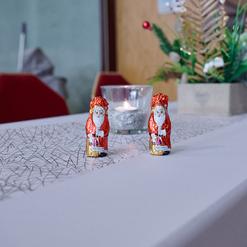 Zwei Schokoladen-Weihnachtsm&auml;nner stehen auf einem festlich gedeckten Tisch mit einer Kerze und gr&uuml;nem Dekor.