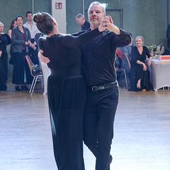 Tanzpaar in eleganter Kleidung tanzt in einer festlichen Umgebung, im Hintergrund Zuschauer auf einer Tanzveranstaltung.