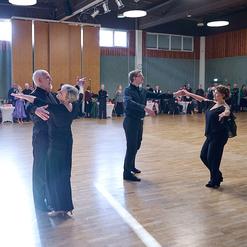 Tanzende Paare in eleganter Kleidung auf einer Tanzfl&auml;che, umgeben von Zuschauern in einem Veranstaltungssaal.