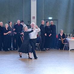 Tanzpaar in eleganter Kleidung auf einer Tanzfl&auml;che, umgeben von Zuschauern in festlicher Atmosph&auml;re.