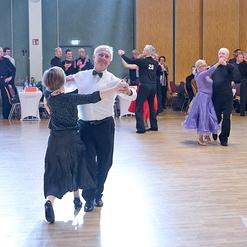 Tanzpaare pr&auml;sentieren sich auf einer Fl&auml;che, umgeben von Zuschauern in einem festlichen Saal.