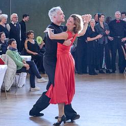 Tanzendes Paar in eleganter Kleidung, umgeben von Zuschauern in einem festlichen Saal.