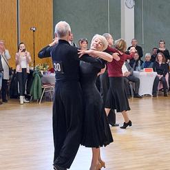 Tanzpaar in eleganter Kleidung tanzt auf einer Veranstaltung, Zuschauer im Hintergrund applaudieren.