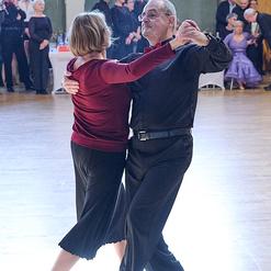 Tanzpaar in eleganter Kleidung, das in einem Festsaal miteinander tanzt, umgeben von begeistertem Publikum.